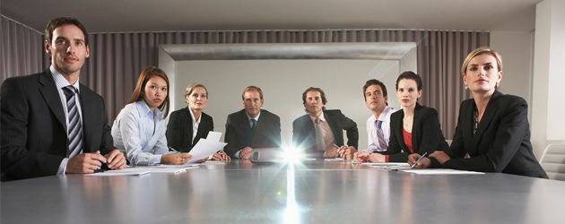 A group of people sitting at a table with one person shining light in the middle.